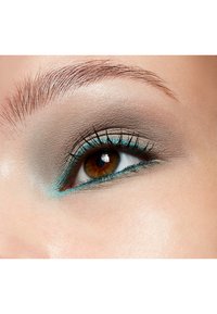 Close-up van een oog met een verloop van neutrale tinten op het ooglid, versterkt door een teal eyeliner en gedefinieerde wimpers. Bruine iris met reflecties.