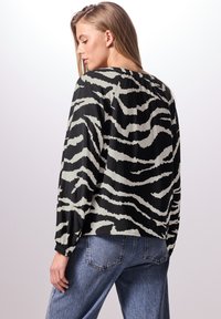 Blouse à manches longues en imprimé zèbre noir et crème, avec un col rond et des poignets élastiqués. Tissu lisse avec une coupe décontractée.