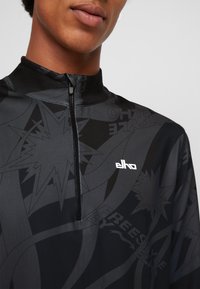 Schwarzes Quarter-Zip Sportoberteil mit strukturierten Mustern und Logo. Es verfügt über einen hohen Kragen und ein elegantes, körperbetontes Design für optimale Leistung.