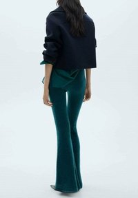Pantaloni a zampa d'elefante realizzati in morbido tessuto teal, abbinati a una giacca cropped scura. Il design presenta un look sartoriale con maniche arrotolate.