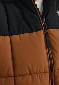 Kurtka ocieplana z czarną górną częścią i brązową dolną częścią, z pełnym zapięciem na zamek i widocznymi szwami na pikowanych panelach.