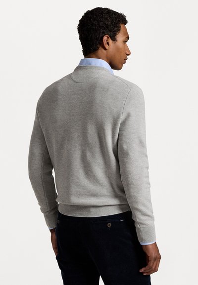 Lys grå strikket genser med teksturert design, ribbestrikket kant og mansjetter. Båret over en lyseblå skjorte med krage, som viser en avslappet silhuett.