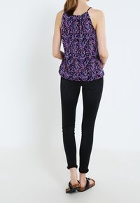 Fioletowa halterka w kwiatowy wzór z marszczonym dekoltem, zestawiona z czarnymi, obcisłymi dżinsami i brązowymi sandałami. Gładki materiał, casualowy styl.