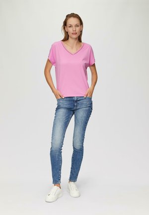 Rosa Kurzarmoberteil mit V-Ausschnitt, kombiniert mit hellblauen Skinny-Jeans und weißen Sneakers. Glatte Textur, lässige Passform.