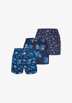Drei Paare dunkelblaue Herrenboxershorts mit tropischen, floralen und abstrakten Mustern, überlappend angeordnet vor weißem Hintergrund.