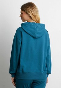 Felpa con cappuccio verde acqua, con polsini e orlo a costine. Materiale in cotone morbido, vestibilità ampia e cappuccio spazioso. Design semplice, senza motivi visibili.