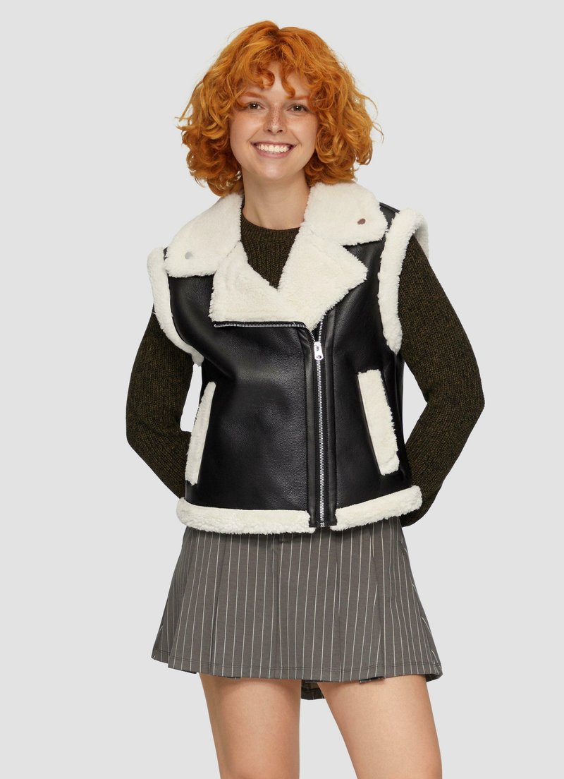 Schwarze Kunstlederweste mit weißen Lammfellakzenten, ausgestattet mit einem Reverskragen, einem Reißverschluss vorne und seitlichen Patschentaschen, getragen über einem Strickpullover.