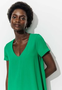 Robe verte avec un décolleté en V et des manches courtes roulées, fabriquée dans un tissu lisse, présentant une silhouette décontractée et peu de détails.