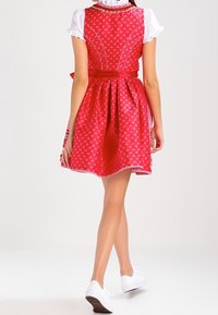 Robe rouge à motif floral, corsage ajusté, jupe évasée et accents blancs. Associée à des chaussures blanches. Texture de tissu lisse.