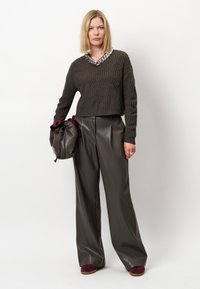 Afgeknipte bruine gebreide trui met een gestructureerd patroon, gecombineerd met hoog getailleerde, wijd uitlopende donkere leren broek. Accessoires omvatten een zachte tas.