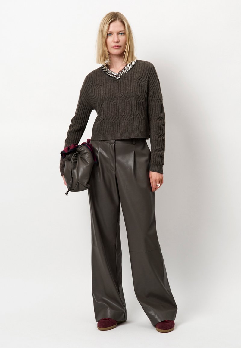 Afgeknipte bruine gebreide trui met een gestructureerd patroon, gecombineerd met hoog getailleerde, wijd uitlopende donkere leren broek. Accessoires omvatten een zachte tas.