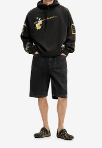 Felpa nera con stampe grafiche e accenti gialli, abbinata a pantaloncini di denim neri e calzature nere con motivo, caratterizzata da una vestibilità comoda.