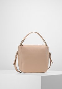 Kompaktní béžová kožená kabelka s vrchním uchem a nastavitelným ramenním páskem, vystavená na bílém podstavci na jednobarevném pozadí.