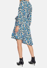 Modelka ubrana w kwiecistą sukienkę w odcieniach niebieskiego, różowego i białego, zestawioną z czarnymi botkami za kostkę, prezentująca profil boczny.