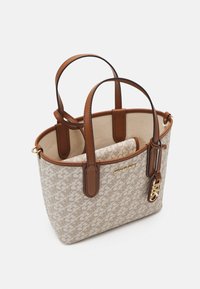 Beige ja ruskea Michael Kors -kassi, jossa on kaksinkertaiset kahvat, sisäinen liukupussi ja kultainen MK-logo-ristikkokoriste sivussa.