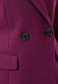 Giacca doppiopetto in tessuto viola profondo con due bottoni neri, un colletto sartoriale e un elegante dettaglio sulla tasca.