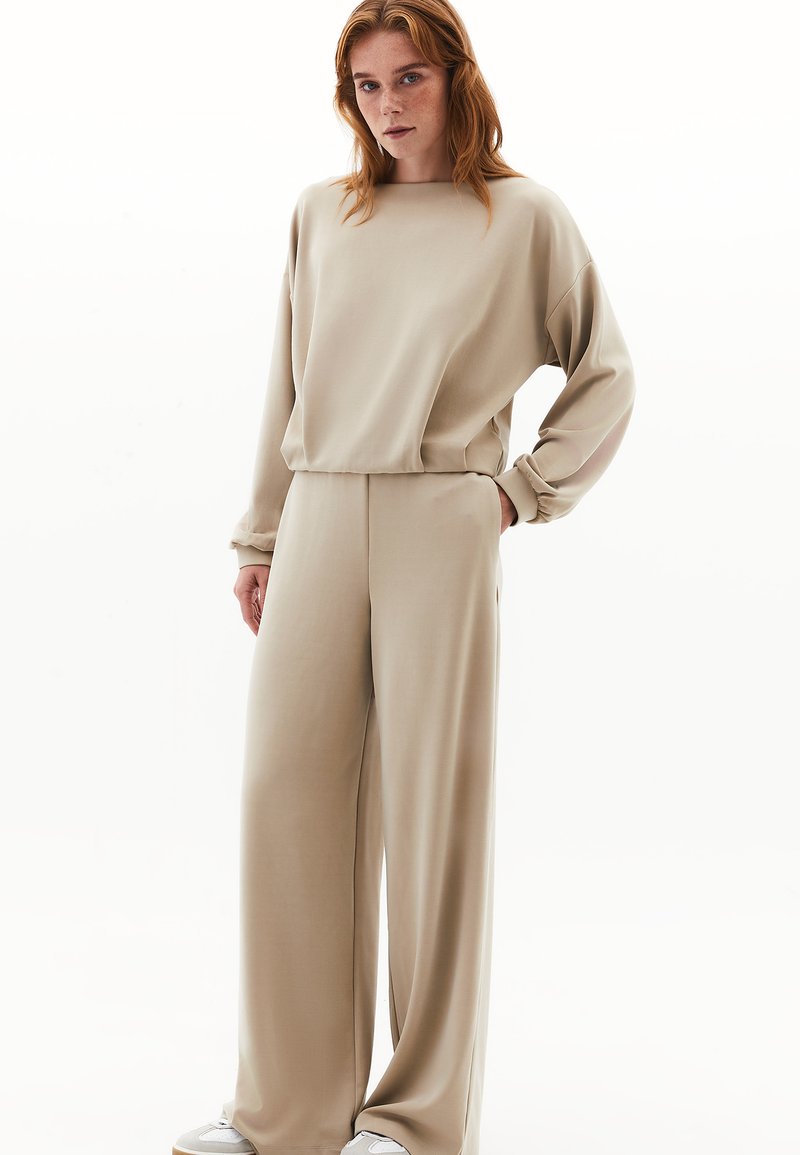 Conjunto de ropa de casa en color beige que incluye una camiseta de manga larga con un ajuste holgado y puños elásticos, combinada con pantalones de pierna amplia. Tejido suave y suave.