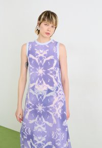 Fialové bezrukoavé šaty s jemným abstraktním vzorem, hladkou teksturou a kulatým výstřihem. Doplňky zahrnují jemný květinový design.
