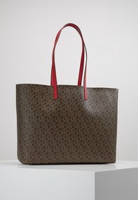 Brun mönstrad axelväska med röda axelremmar. Tillverkad av hållbart material, den har en rymlig design för praktisk användning.