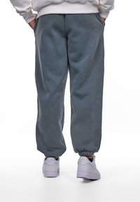 Grå sweatpants med elastiske manchetter, lavet af blødt stof, med sidelommer og en afslappet pasform, parret med hvide sneakers.