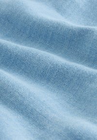 Tissu tissé bleu clair avec une texture douce et des fils fins visibles formant un motif subtil en quadrillage.