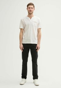 Lichtgekleurde kortemouwen shirt met V-hals en een borstzak, gecombineerd met zwarte broek en witte sneakers. Eenvoudig ontwerp en textuur.