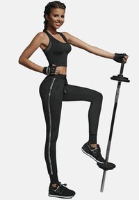 Czarny sportowy top cropped i dresy z srebrnymi bocznymi paskami, w połączeniu z czarnymi sneakersami. Model pozuje z sztangą, prezentując odzież fitness.