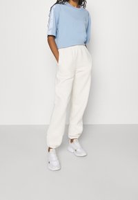 Ljusblå kortärmad t-shirt med tre vita ränder på ärmarna, kombinerad med löst sittande vita sweatpants och vita sneakers.