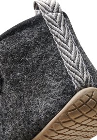 Gros plan d'une pantoufle en feutre gris foncé avec une semelle en caoutchouc beige et une languette grise et blanche à motif chevrons.