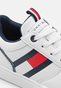 Białe skórzane sneakersy z granatowymi i czerwonymi akcentami, teksturowanym overlayem, granatowym wykończeniem wnętrza oraz oznakowanym językiem. Okrągły czubek i płaska podeszwa.