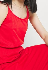 Haut caraco rouge en tissu doux et léger, doté de fines bretelles et d'une coupe décontractée, accompagné d'une jupe rouge assortie.