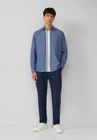 Camicia blu a fantasia con bottoni e taschino frontale, abbinata a pantaloni blu scuro e sneakers bianche. Vestibilità slim; maniche lunghe, stile casual.
