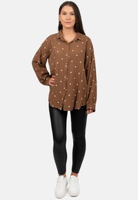 Brown button-up shirt with white heart patterns, long sleeves, and a relaxed fit, paired with black leggings and white sneakers.