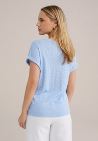 Haut bleu clair à manches courtes avec un motif chevron texturé, col rond et manches repliées, fabriqué à partir d'un tissu doux et respirant.