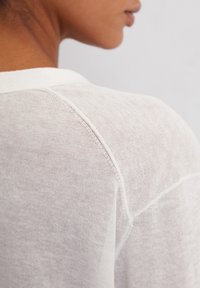 Hellbeige Strickpullover mit rundem Halsausschnitt, kurzen Ärmeln und einem strukturierten, weichen Stoff mit sichtbaren Nähten.