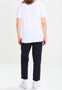T-shirt en coton blanc à manches courtes, associé à un pantalon bleu marine évasé. La tenue est complétée par des baskets blanches et des poignets retroussés visibles.