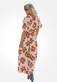 Roomkleurige maxi-jurk met grote oranje bloemen, korte mouwen, elastische taille en een losse pasvorm, gecombineerd met nude hakken.