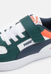 Baskets teal et blanches avec une bande Velcro, dotées d'une finition texturée, de lacets blancs, d'accents navy et d'un logo de marque sur le côté.