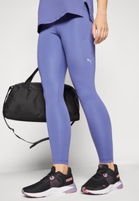 Leggings violettes moulantes en tissu extensible, assorties à des chaussures de sport noires avec des accents roses et un sac de sport noir.
