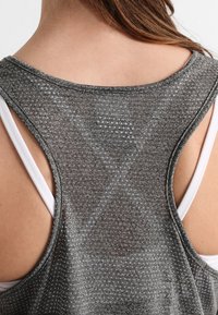Lichtgewicht grijze tanktop met een gestructureerd patroon, met een racerback-ontwerp en in laagjes over een witte bh.