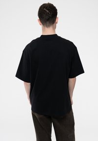Black oversized t-shirt made of cotton, featuring short sleeves and a round neck. The back view shows a plain design with no visible branding.