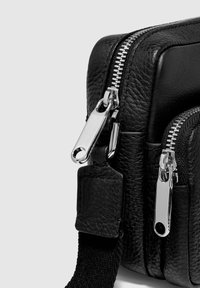 Svart läderväska med silverfärgade dragkedjor, strukturerad yta, dubbla fack och justerbar rem. Utrustad med en platt, präglad etikett.