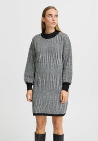 Strickkleid im Schwarz-Weiß Fischgrätmuster, mit hohem Rundhalsausschnitt und langen Ballonärmeln mit gerippten Bündchen.