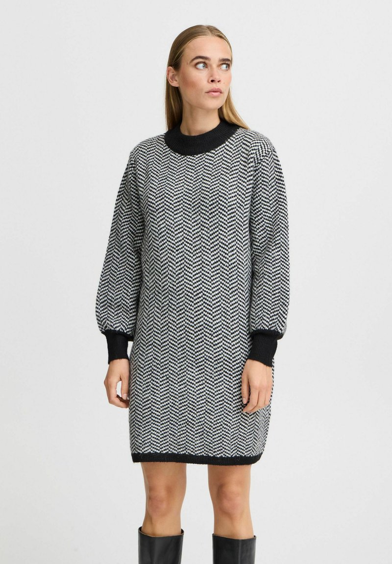 Strickkleid im Schwarz-Weiß Fischgrätmuster, mit hohem Rundhalsausschnitt und langen Ballonärmeln mit gerippten Bündchen.