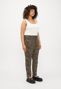 Bílý tílko bez rukávů spárované s černými kalhotami s designem vzoru leopardu. Modelka má na sobě masivní černé platformové boty.