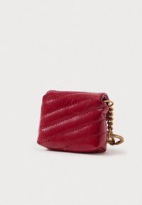 Bolsa de couro acolchoado vermelho com um detalhe em corrente dourada e forma arredondada, apresentando padrões diagonais em relevo e uma superfície plana e lisa.