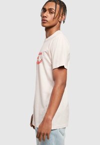 Light pink cotton t-shirt featuring short sleeves and a crew neckline, with red text printed on the front. The fit is relaxed.