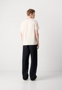 Lys beige bomulls T-skjorte med rund hals, båret med løstsittende mørkeblå bukser. Stoffet ser mykt og uformelt ut.