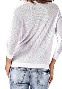 Pull en maille blanche avec un design en maille ouverte, manches trois-quarts et poignets côtelés, associé à un jean bleu délavé avec poches arrière.