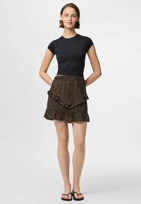 Juodas trumpos rankovės viršus derinamas su rudą sluoksniuotą sijoną su Volanais. Sijonas turi elastinį juosmenį ir nėrinių akcentus. Ant kojų avimos juodos šlepetės.